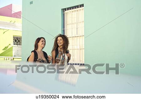 Picture - Young women walking past pastel painted house. Fotosearch