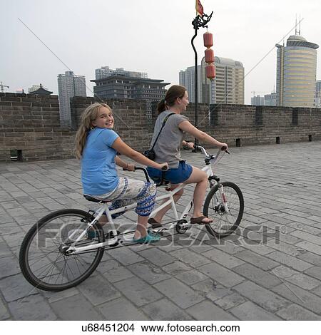 Picture - Happy mother and daughter riding tandem bicycle at Xian City Wall, Xi'an, Shaanxi, China.. Fotosearch