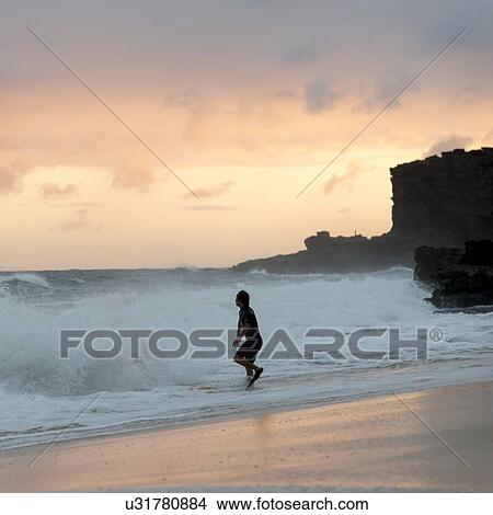 Picture - Man playing with waves on the beach at sunset, Sandy Beach, Hawaii Kai, Honolulu, Oahu, Hawaii, USA. Fotosearch