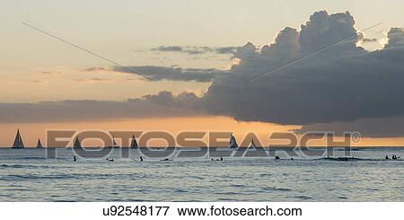 Stock Photo - Surfers and sailboats in the ocean at sunset, Waikiki, Honolulu, Oahu, Hawaii, USA. Fotosearch