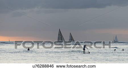 Stock Photograph - Surfers in the ocean with sailboats in the background, Waikiki, Honolulu, Oahu, Hawaii, USA. Fotosearch