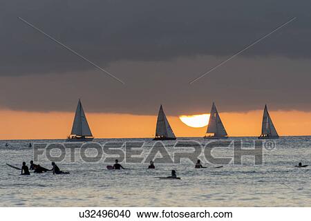 Surfers on the beach with sailboats in the background at sunset, Waikiki, Honolulu, Oahu, Hawaii, USA View Large Photo Image Stock Image - Surfers on the beach with sailboats in the background at sunset, Waikiki, Honolulu, Oahu, Hawaii, USA. Fotosearch
