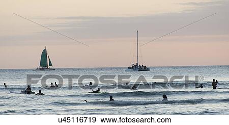 Stock Photo - Surfers with sailboats in the background at sunset, Waikiki, Honolulu, Oahu, Hawaii, USA. Fotosearch