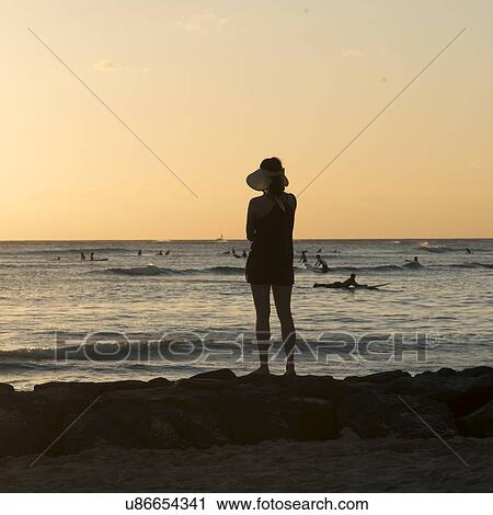 Stock Image - Woman looking at surfers on the beach, Waikiki, Honolulu, Oahu, Hawaii, USA. Fotosearch