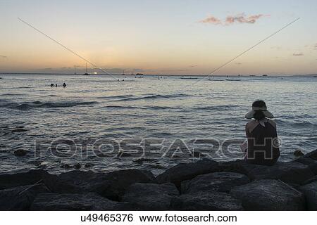 Woman sitting on the beach at sunset, Waikiki, Honolulu, Oahu, Hawaii, USA View Large Photo Image Stock Photograph - Woman sitting on the beach at sunset, Waikiki, Honolulu, Oahu, Hawaii, USA. Fotosearch