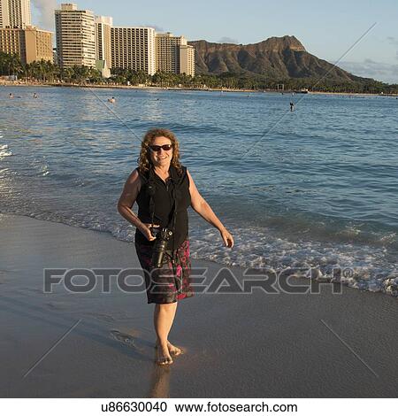 Stock Image - Woman smiling with holding a camera on the beach, Waikiki, Honolulu, Oahu, Hawaii, USA. Fotosearch