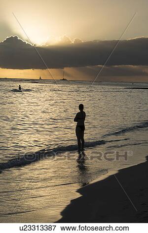Stock Photo - Woman standing on beach and looking at ocean sunset, Waikiki, Honolulu, Oahu, Hawaii, USA. Fotosearch