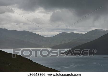 Stock Photograph - Yamdrok Lake with mountains under cloudy sky, Nagarze, Shannan, Tibet, China. Fotosearch