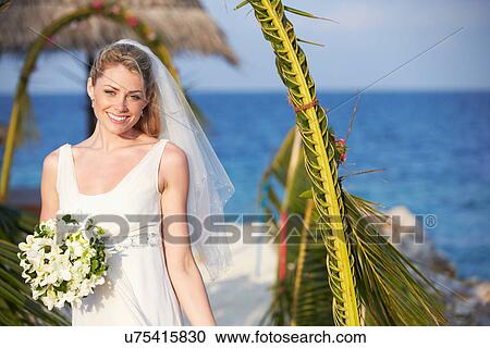 Stock Image - Beautiful Bride Getting Married In Beach Ceremony. Fotosearch