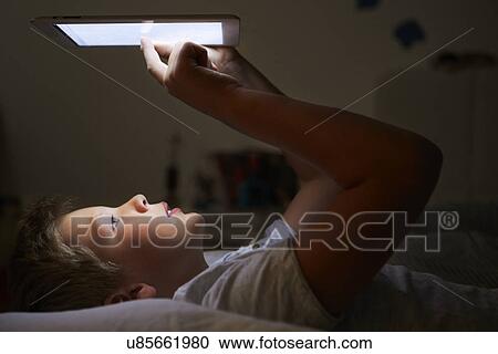 Stock Image - Boy Looking At Digital Tablet In Bed At Night. Fotosearch