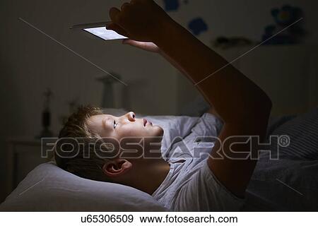 Stock Photo - Boy Looking At Digital Tablet In Bed At Night. Fotosearch