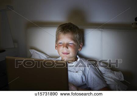 Stock Image - Boy Using Laptop In Bed At Night. Fotosearch
