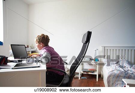 Stock Image - Boy Using Laptop In Bedroom. Fotosearch
