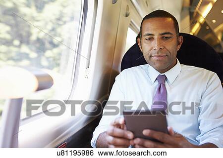 Stock Photograph - Businessman Commuting On Train Reading E Book. Fotosearch