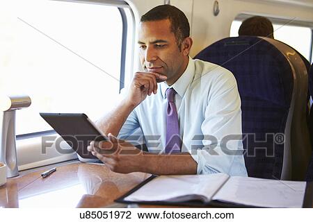 Stock Image - Businessman Commuting On Train Using Digital Tablet. Fotosearch