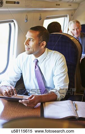 Stock Photography - Businessman Commuting On Train Using Digital Tablet. Fotosearch