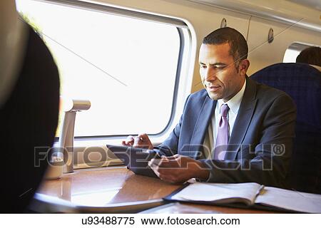 Stock Photography - Businessman Commuting On Train Using Digital Tablet. Fotosearch