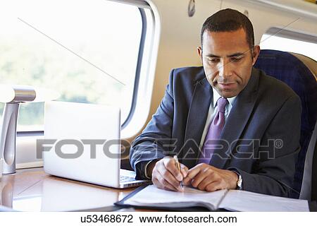 Stock Image - Businessman Commuting To Work On Train And Using Laptop. Fotosearch