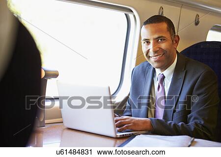 Stock Image - Businessman Commuting To Work On Train And Using Laptop. Fotosearch