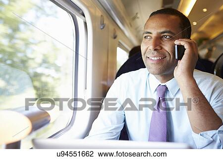 Stock Image - Businessman Commuting To Work On Train Using Mobile Phone. Fotosearch