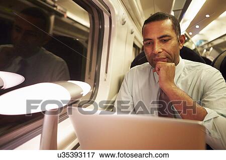 Stock Photo - Businessman Commuting To Work On Train And Using Laptop At Night. Fotosearch