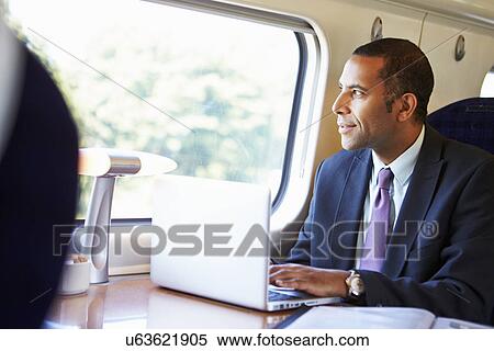 Stock Photography - Businessman Commuting To Work On Train And Using Laptop. Fotosearch