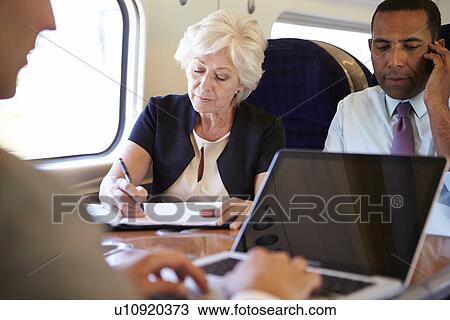 Stock Image - Businesspeople On Train Using Digital Devices. Fotosearch
