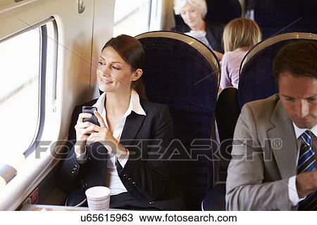 Stock Image - Businesswoman Commuting To Work On Train Using Mobile Phone. Fotosearch