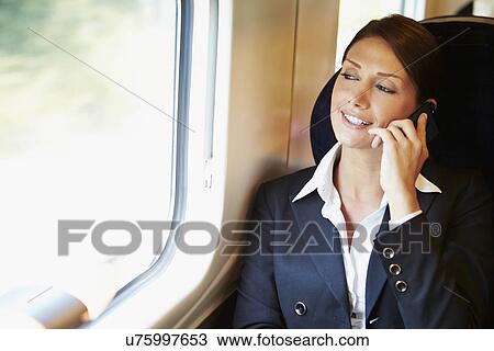 Stock Image - Businesswoman Commuting To Work On Train Using Mobile Phone. Fotosearch