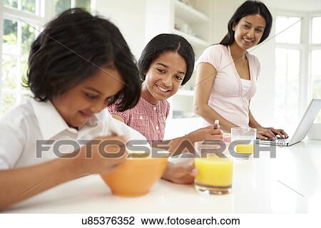 Stock Image - Children Having Breakfast With Mother Before School. Fotosearch