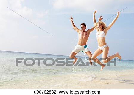 Stock Image - Couple Jumping In The Air On Tropical Beach. Fotosearch