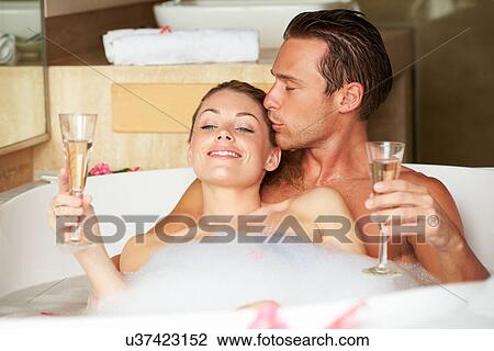 Stock Image - Couple Relaxing In Bath Drinking Champagne Together. Fotosearch