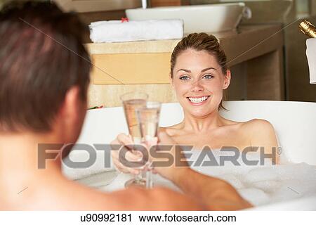 Stock Image - Couple Relaxing In Bath Drinking Champagne Together. Fotosearch