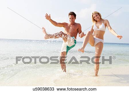 Stock Image - Couple Splashing In Sea On Beach Holiday. Fotosearch