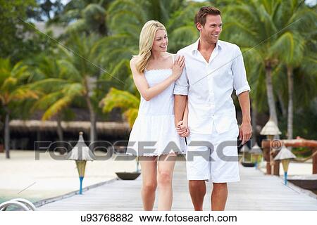 Stock Image - Couple Walking On Wooden Jetty. Fotosearch