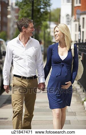 Stock Image - Couple With Pregnant Wife Walking Along Urban Sidewalk. Fotosearch