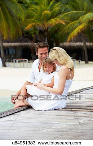 Stock Image - Family Sitting On Wooden Jetty. Fotosearch
