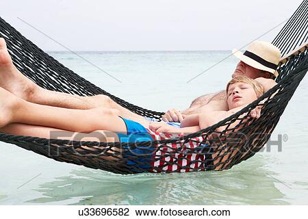Stock Image - Grandfather And Grandson Relaxing In Beach Hammock . Fotosearch
