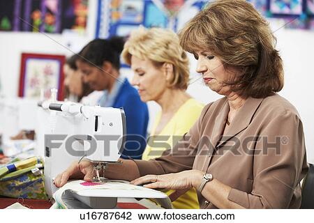 Stock Image - Group Of Women Using Electric Sewing Machines In class. Fotosearch