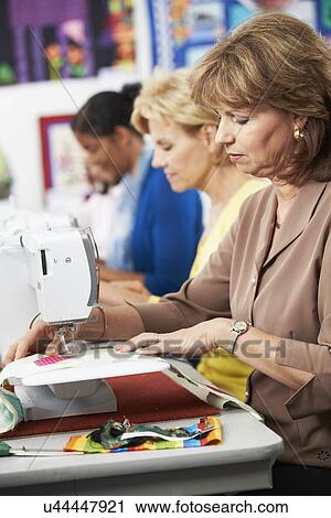 Stock Image - Group Of Women Using Electric Sewing Machines In class. Fotosearch