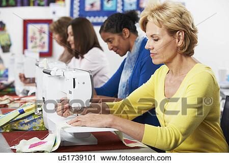 Stock Image - Group Of Women Using Electric Sewing Machines In class. Fotosearch
