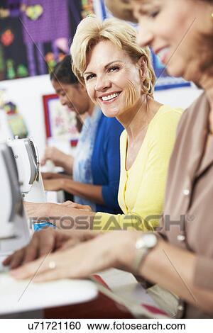 Stock Image - Group Of Women Using Electric Sewing Machines In class. Fotosearch