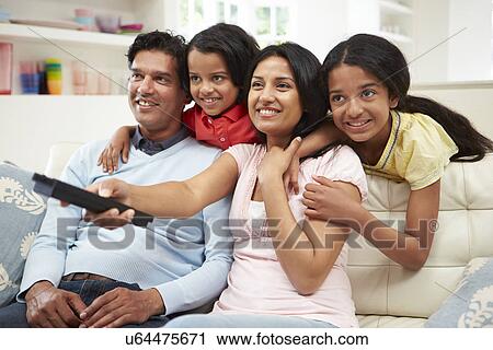 Stock Image - Indian Family Sitting On Sofa Watching TV Together. Fotosearch