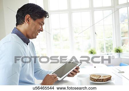 Picture - Indian Man Using Digital Tablet Whilst Eating Breakfast. Fotosearch