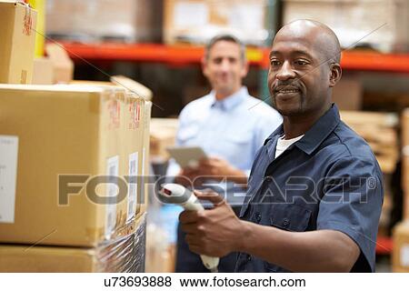 Stock Photo - Manager In Warehouse With Worker Scanning Box In Foreground. Fotosearch