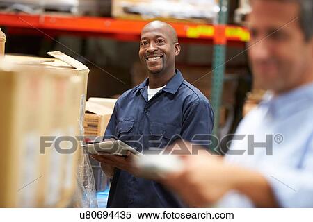 Stock Photography - Manager In Warehouse With Worker Scanning Box In Foreground. Fotosearch