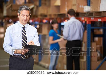 Stock Image - Manager In Warehouse Writing On Clipboard. Fotosearch