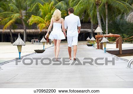 Stock Image - Rear View Of Couple Walking On Wooden Jetty. Fotosearch
