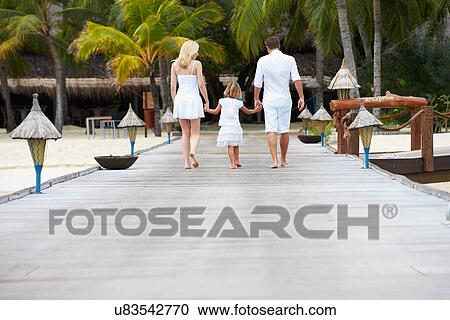 Stock Image - Rear View Of Family Walking On Wooden Jetty. Fotosearch
