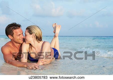 Stock Image - Romantic Couple Lying In Sea On Tropical Beach Holiday. Fotosearch
